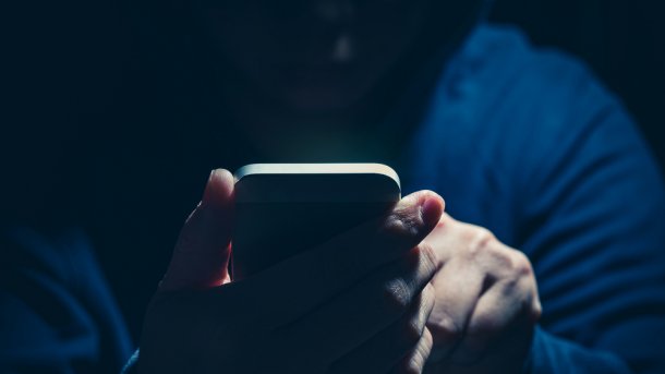 Ein Mann in dunklem Hoodie hält ein Smartphone in der Hand.