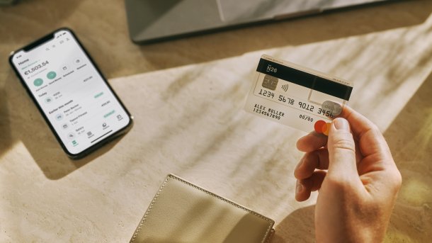 Geldkarte von N26 in einer Hand, auf dem Tisch im Hintergrund ein Smartphone mit der App der Bank