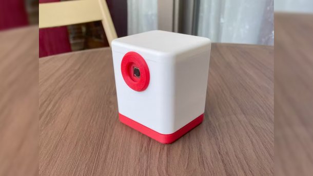 Eine rot-weiße Kamera steht auf einem Tisch. Die Linse zeigt schräg nach vorn.