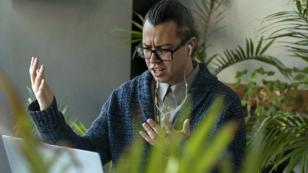 Verärgert User mit Brille sitzt vor einem Laptop und hebt verzweifelt die Arme