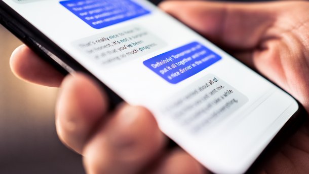 A smartphone with an open messaging app in a human hand, a chat can be seen blurred on the screen.