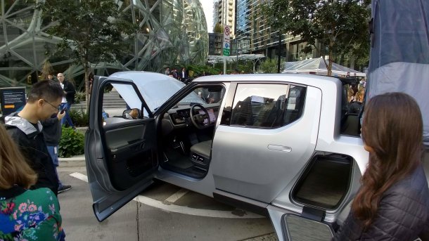 A prototype Rivian pickup truck is on display with its door and hood open in front of the Amazon headquarters in Seattle