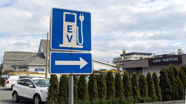 A road sign points the way to a charging station for electric cars. In the photo, the arrow also points to a restaurant called "Good Fortune".