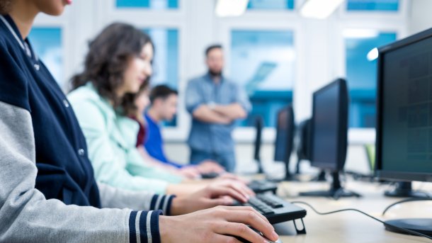 Several students sit in a row at computers