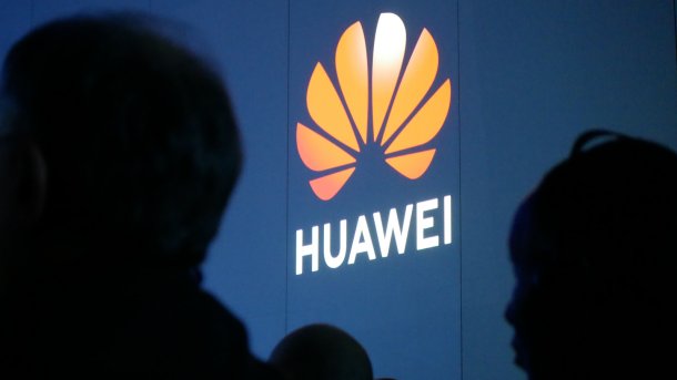 Das Huawei-Logo an eine Wand projiziert; im Vordergrund Schattenrisse zweier Menschen
