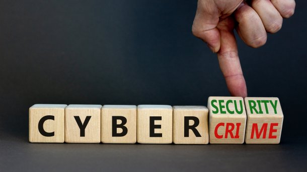 Cubes with letters spell out "CYBERCRIME"; a Finge is turning some letters around to make it "CYBERSECURITY".