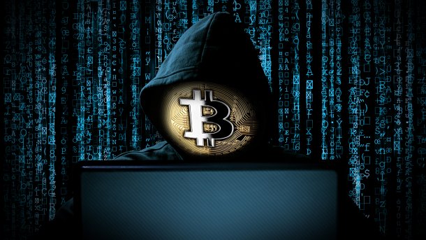 Hacker mit Hoodie und Bitcoin-Maske vor einem Laptop