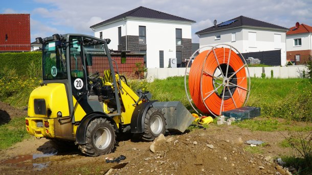 Baustelle eines Neubaugebiets in Barsinghausen bei Hannover, im Vordergrund ein kleiner Bagger und eine Rolle Glasfaserkabel.