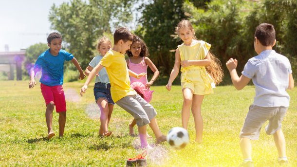 Kinder spielen glücklich auf einer grünen Wiese mit einem Fußball.