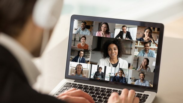 Mann mit Kopfhörern vor Laptop mit Videkonferenz