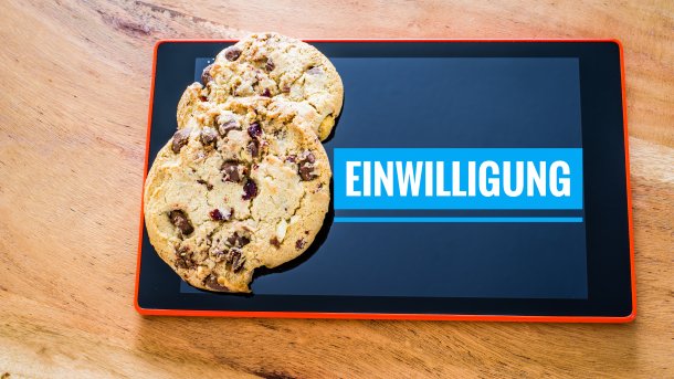 Ein Tablet zeigt das Wort "Einwilligung" an; auf dem Tablet liegen zwei Kekse