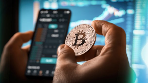 Hand with Bitcoin in front of trading app