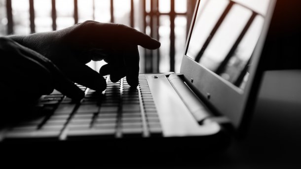 Hände am Laptop im Gegenlicht, Vordergrund im Dunklen