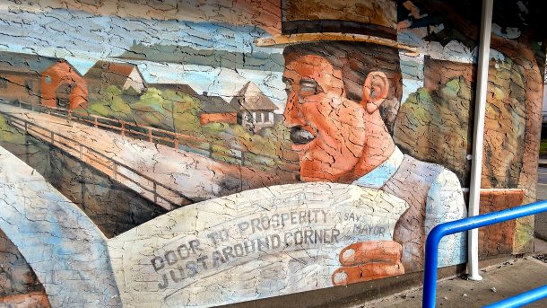 Wandgemälde; Mann liest Zeitung mit Schlagzeile "Door to Prosperity just around corner, says mayor"