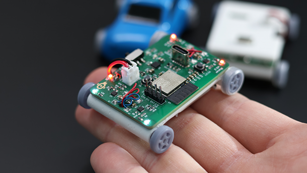 Ein handtellergroßes Auto wird auf einer Hand präsentiert. Es besteht aus einer flachen 3D-Karosserie, auf der ein PCB befestigt ist.
