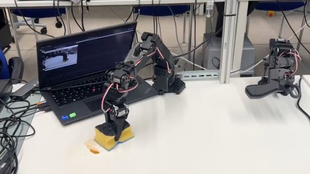 Robot arm in front of notebook cleans spilled liquid from a table.