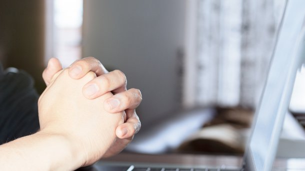 Mann mit zusammengefalteten Händen vor einem Laptop