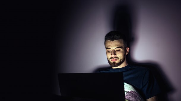 Man mit Laptop auf dem Schoß, beleuchtet nur durch den Monitor