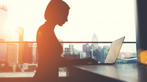 Silhouette einer Frau am Laptop vor der Kulisse einer Großstadt mit Wolkenkratzern