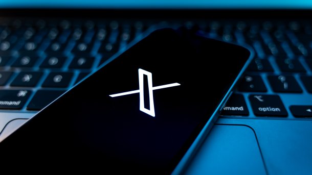 X symbol on a smartphone. The smartphone is placed on a Mac notebook keyboard.