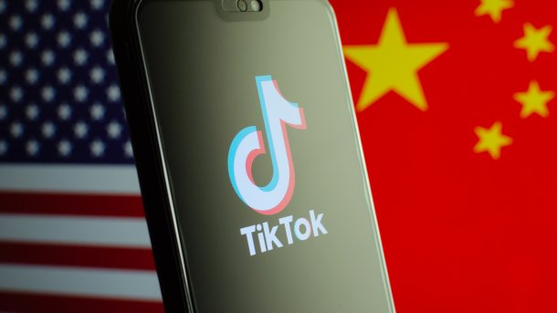 TikTok-Logo auf einem Smartphone, im Hintergrund die Flaggen der USA und Chinas