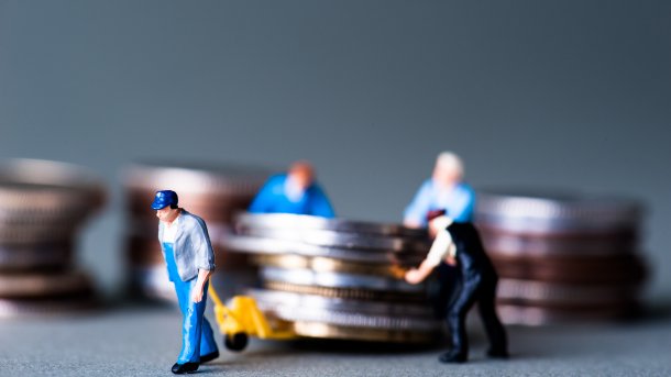 Miniaturfiguren verschieben einen Stoß Münzen