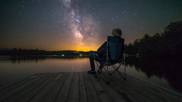 Man sitting on a camping chair on a jetty under the starry sky