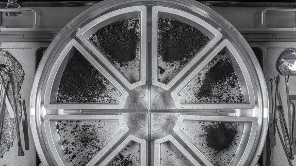 A semicircular container with several compartments containing black material