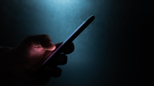 In einem dunklen Raum hält eine Hand ein Handy