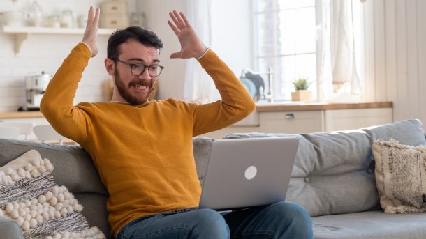 Frustrierter Mann mit hocherhobenen Händen und einem Laptop auf dem Schoß