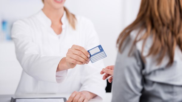 Blonde doctor in a white coat gives patients their health insurance card. 