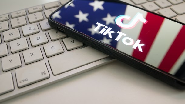Ein Smartphone auf einer Tastatur, im Display mit dem TikTok-Schriftzug spiegelt sich die US-Flagge 