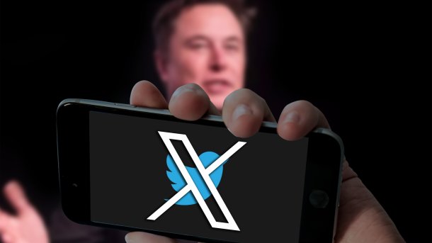 Blurred Elon Musk behind smartphone with X logo in front of Twitter bird