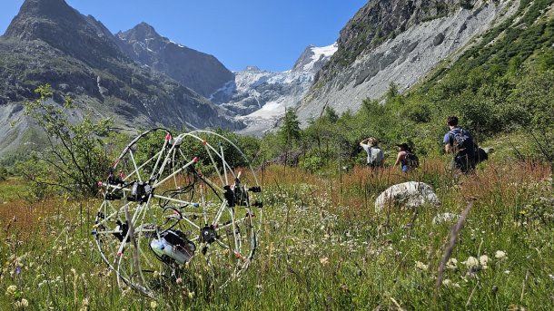 Shape-changing robot GOAT rolls down a hill in an Alpine landscape.