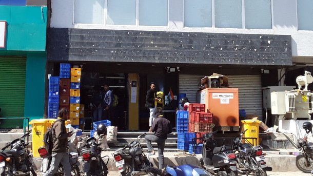 Eingang in ein Geschäftslokal ohne Aufschrift; davor Kisten, Motoroller und ein paar junge Inder