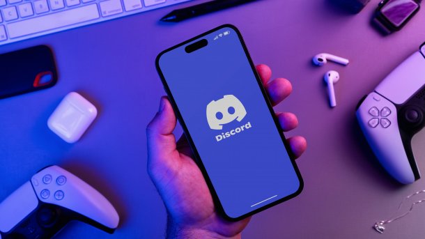 Smartphone mit Discord-App darauf, im Hintergrund Controller und Tastatur
