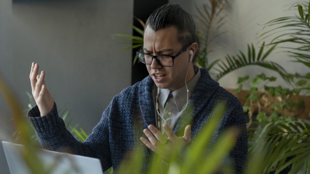 Verärgert User mit Brille sitzt vor einem Laptop und hebt verzweifelt die Arme