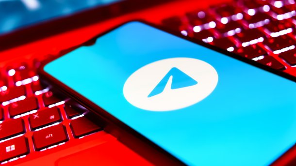 Logo von Telegram auf einem Smartphone, das auf einer rot leuchtenden Tastatur liegt