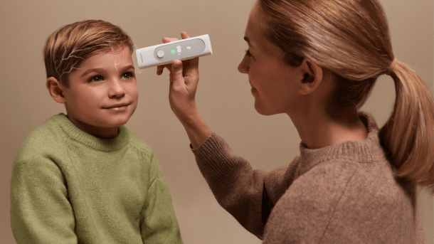 A woman holds a white stick to the forehead of a boy