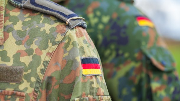 Shoulder of a soldier of the Bundeswehr in a spotted camouflage suit with epaulette and German flag on the upper arm. 