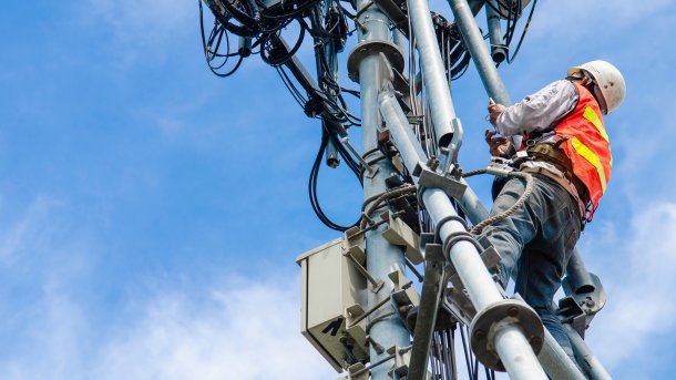 A technician in protective clothing carries out work at the top of an antenna mast with mobile phone antennas.