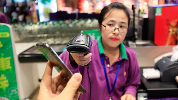 Eine Kassiererin scannt den QR-Code einer Bezahl-App von einem Handy.