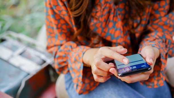 Frau mit Smartphone in der Hand, auf dem Facebook geöffnet ist