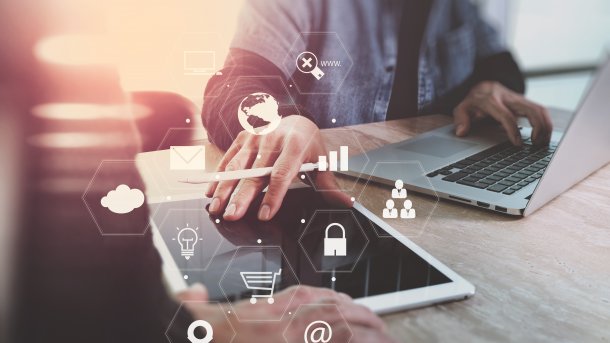 Verschiedene Symbole zu vernetzten Geräten, im Hintergrund zwei Personen gegenübersitzend, in der Mitte ein Tablet