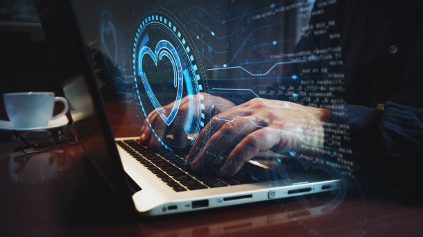 Eine Grafik zeigt zwei Hände, die auf einer Laptop-Tastatur tippen, über den Händen wurde ein Herz-Symbol hineinretouchiert.