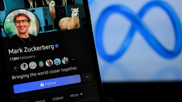 Photo of a cell phone with Mark Zuckerberg's Facebook profile. The Meta logo in the background.