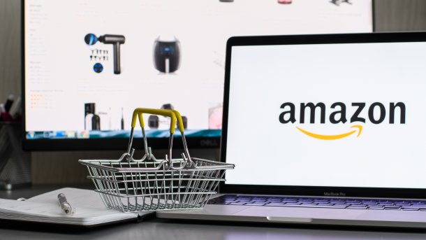 Miniature shopping basket to the left of a laptop with the Amazon logo. In the background are the Amazon Buy Boxes, in which products are placed on the website of the online giant Amazon.