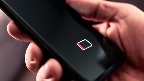 Smartphone mit dem Symbol für leeren Akku in einer Hand