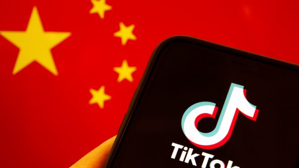 TikTok-Logo auf einem Smartphone, im Hintergrund die Flaggen der USA und Chinas