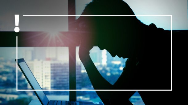 Eine Person sitzt in gebeugter Haltung vor einem Laptop.